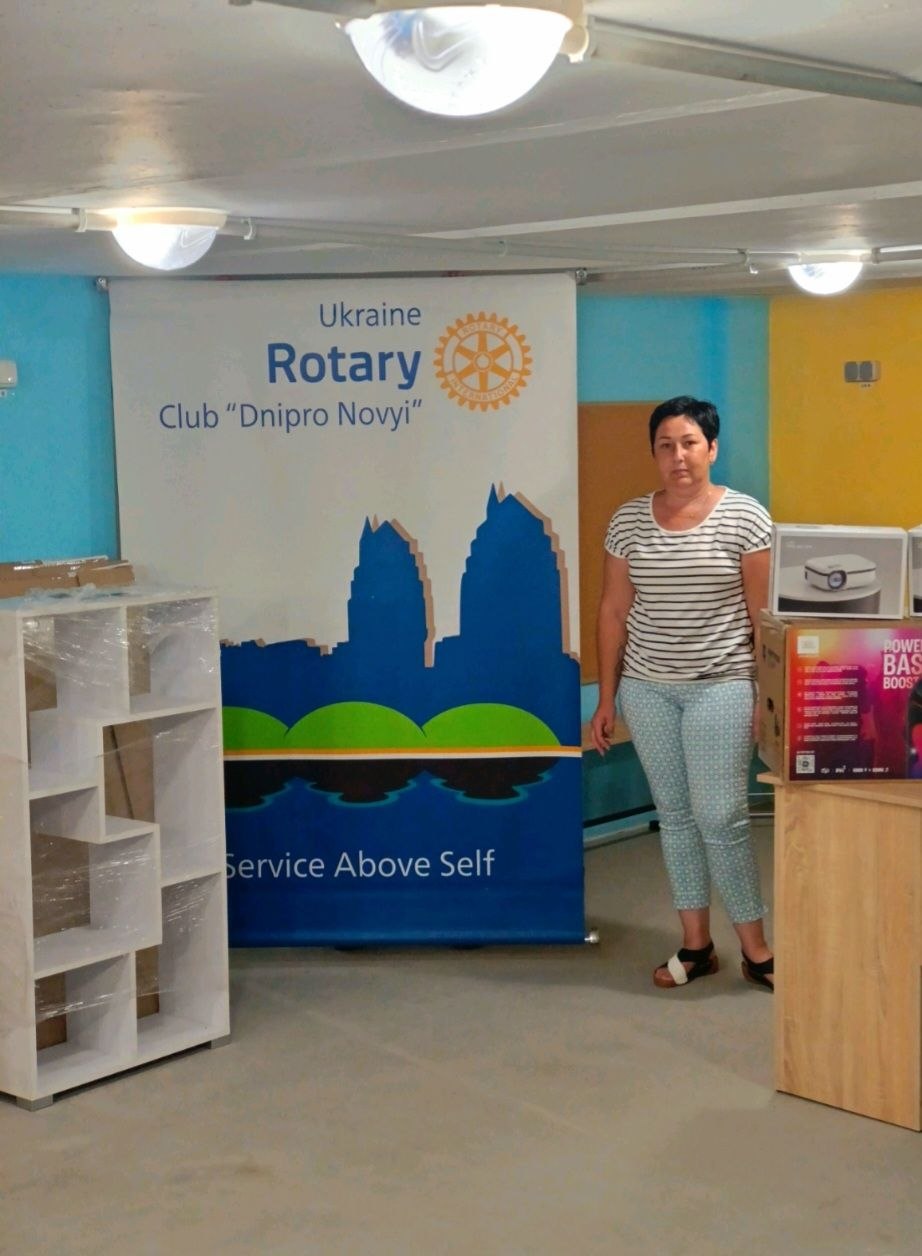 A woman from Vyvodove standing beside the Rotary Club of Dnipro Novyi banner inside the newly outfitted underground space, August 2026.