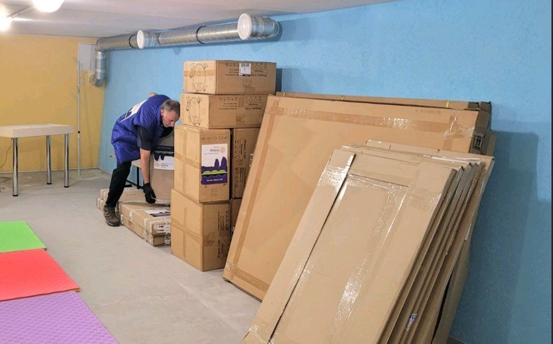 A Rotarian moving delivered boxes into the finished underground space at Vyvodove, August 2026.