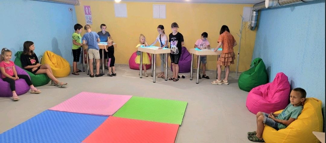 Children working at two illuminated therapy tables in the finished underground space at Vyvodove Gymnasium, August 2026.